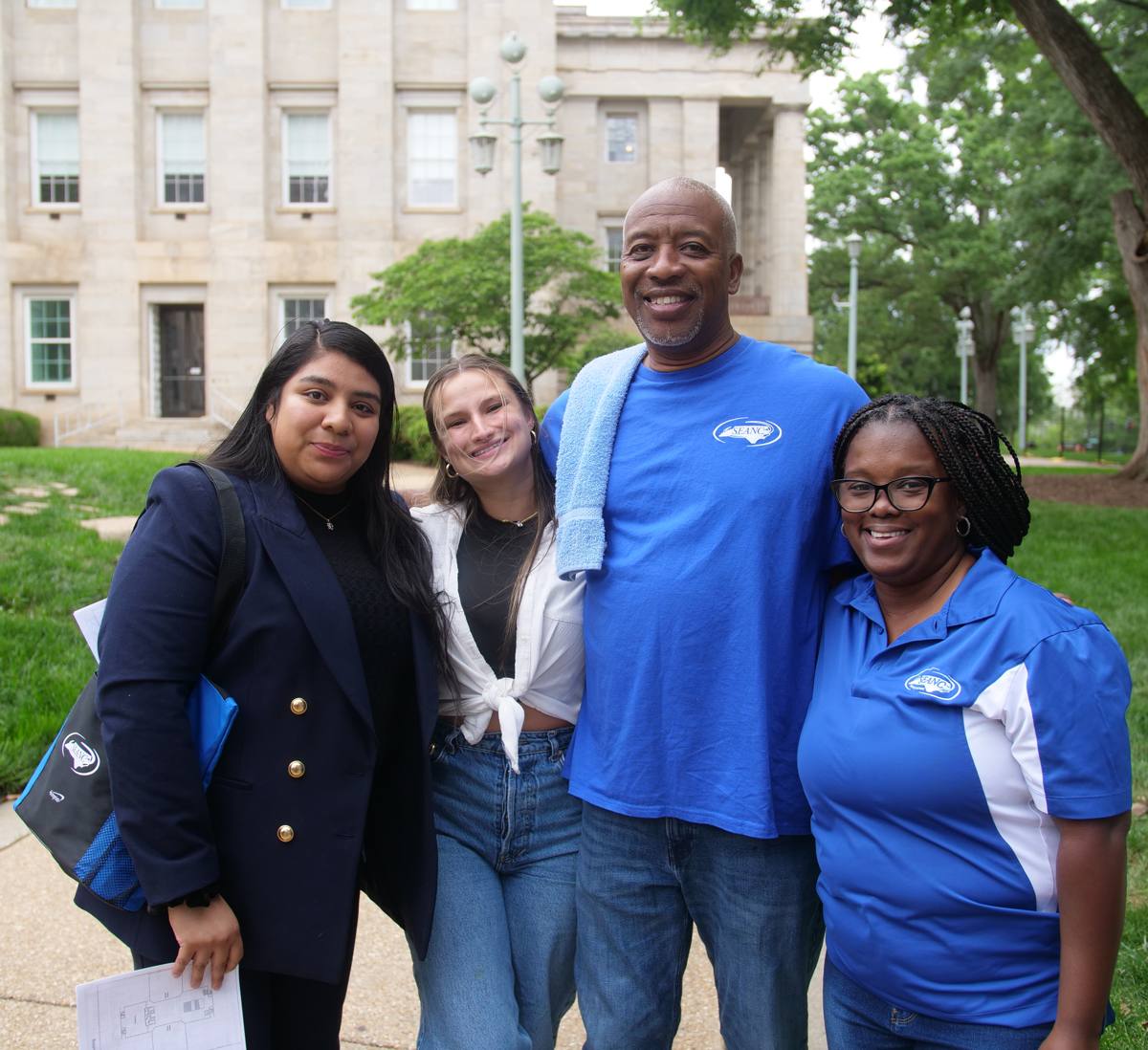 Four SEANC members in blue SEANC shirts smiling in front of the N.C. State Capitol